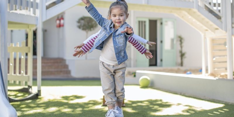 Girls at preschool, portrait balancing on balance beam in garden